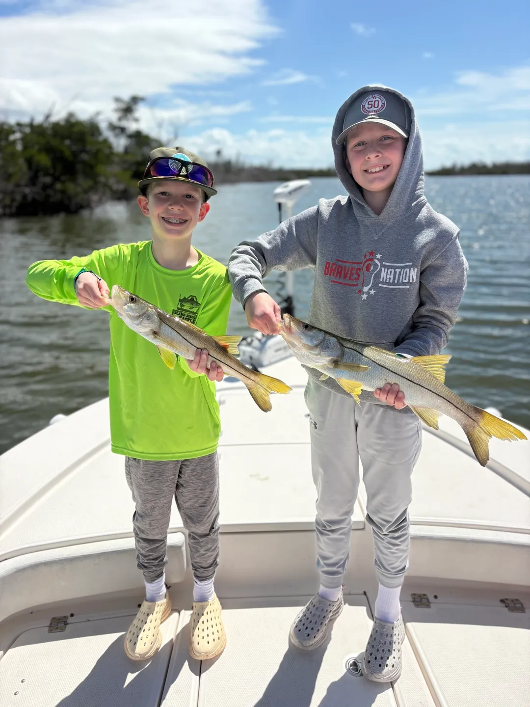 Two kids proudly holding fish on boat.