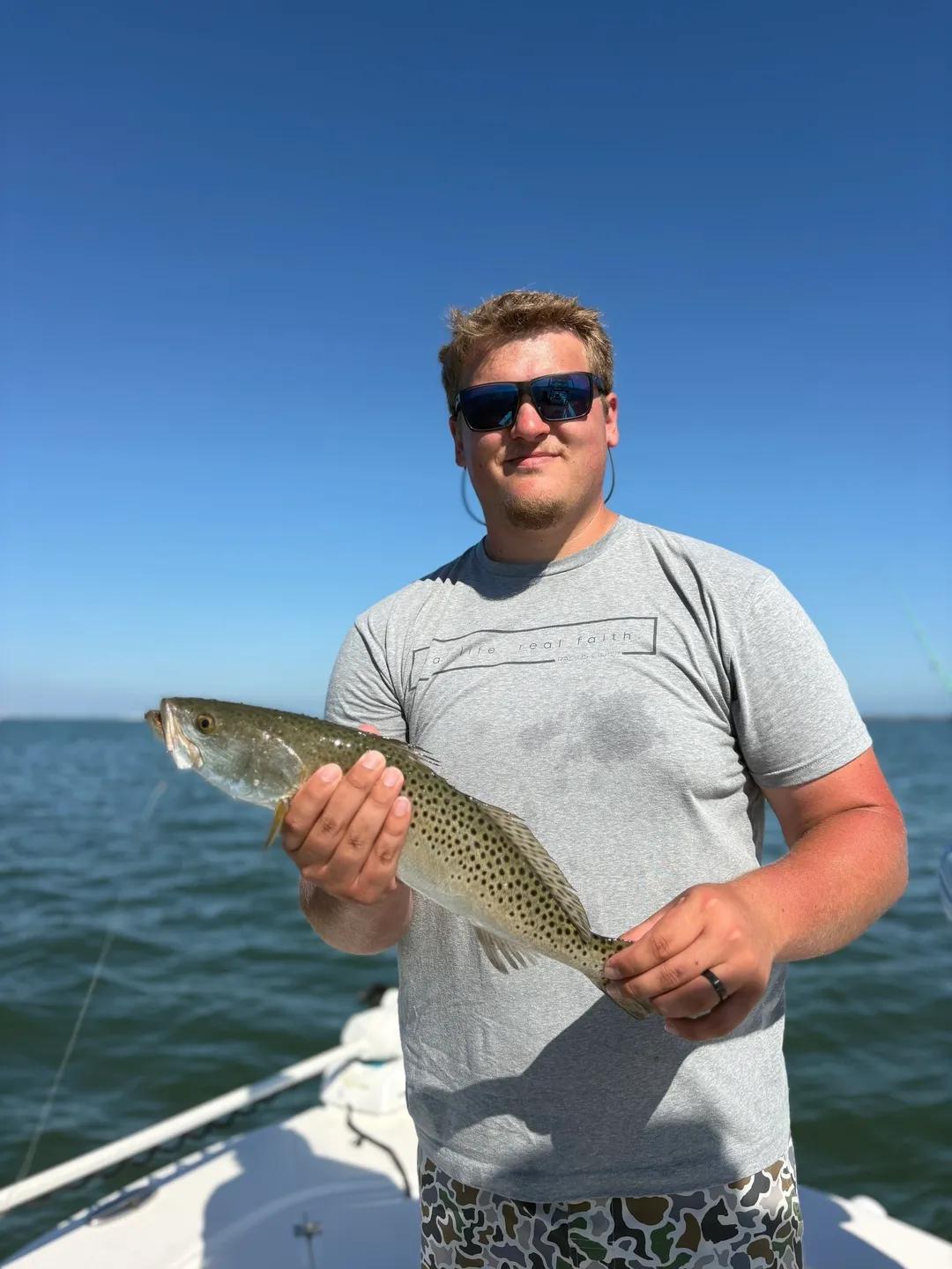 Angler with trout against blue sky.